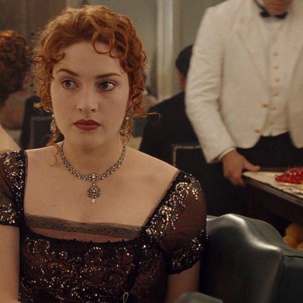 a woman sitting at a table with a cake in front of her and two other people standing behind her