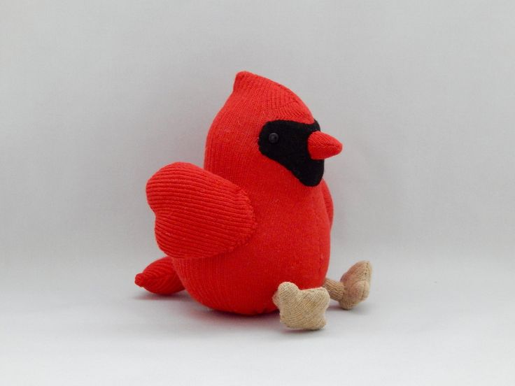 a red stuffed bird sitting on top of a white floor next to a small bone