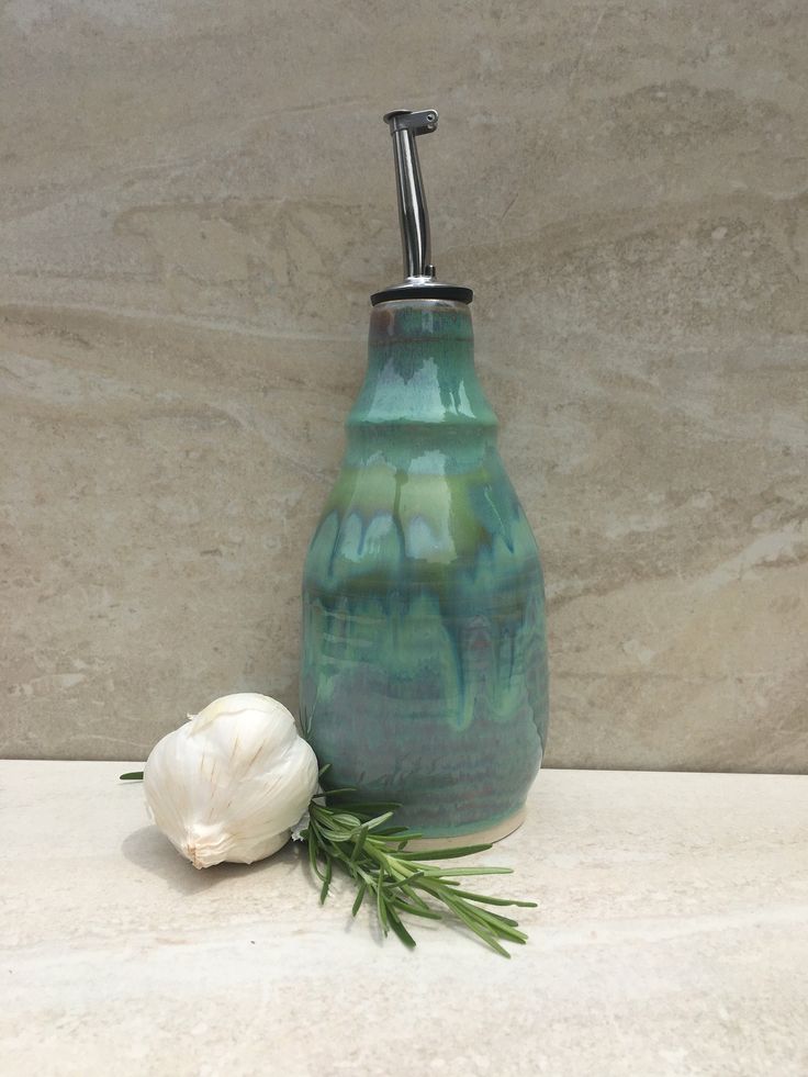 a green vase sitting on top of a counter next to a white flower and a faucet