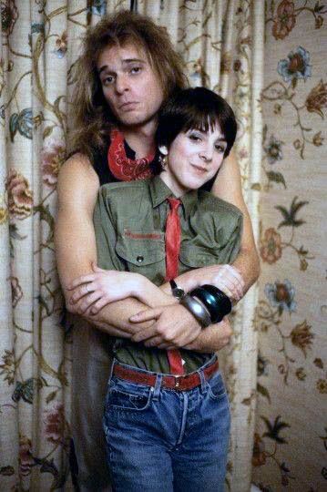 a man and woman standing next to each other in front of curtains with floral designs on them