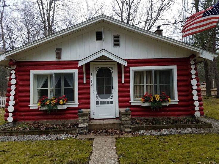 a small red and white house with flowers on the front porch, and an american flag flying outside