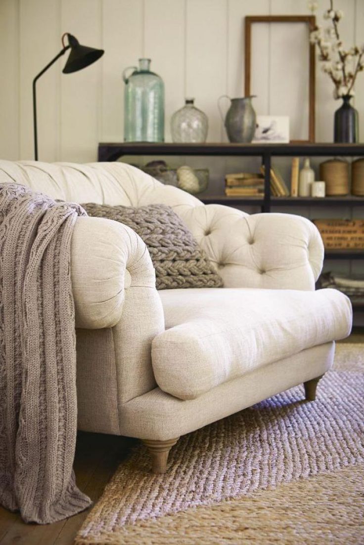 a white couch sitting on top of a wooden floor next to a lamp and bookshelf