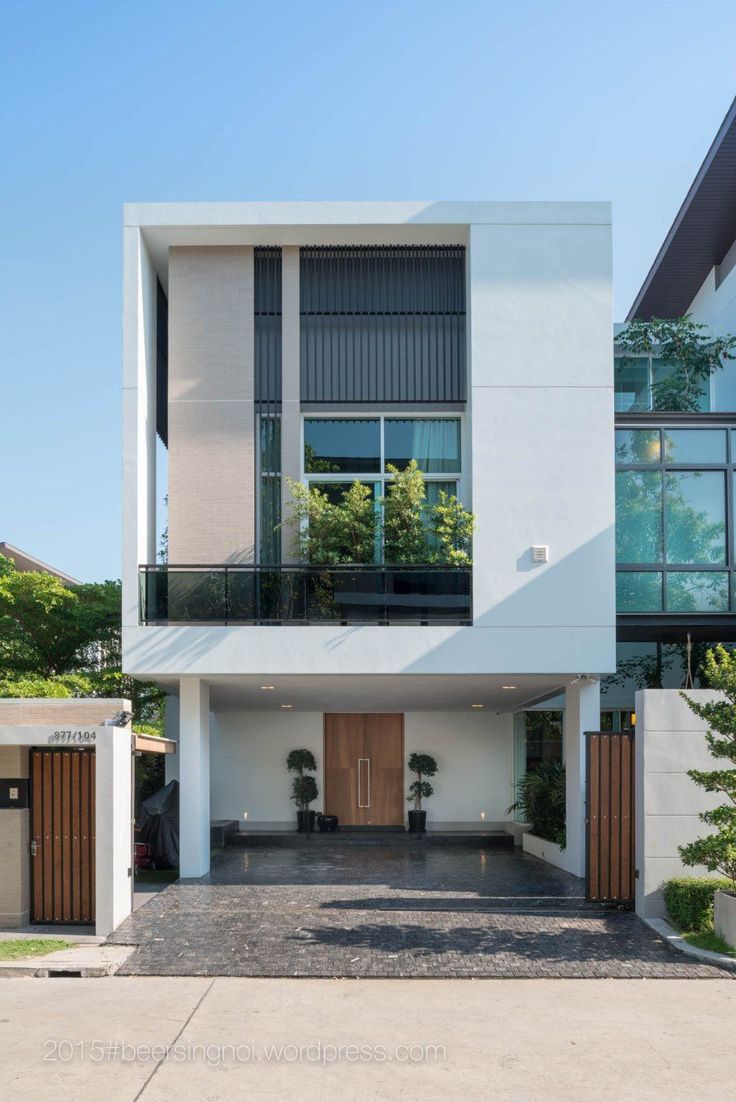 a modern house with white walls and wooden doors on the second floor, surrounded by greenery