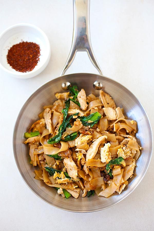 a silver bowl filled with noodles and vegetables next to a small white bowl full of seasoning