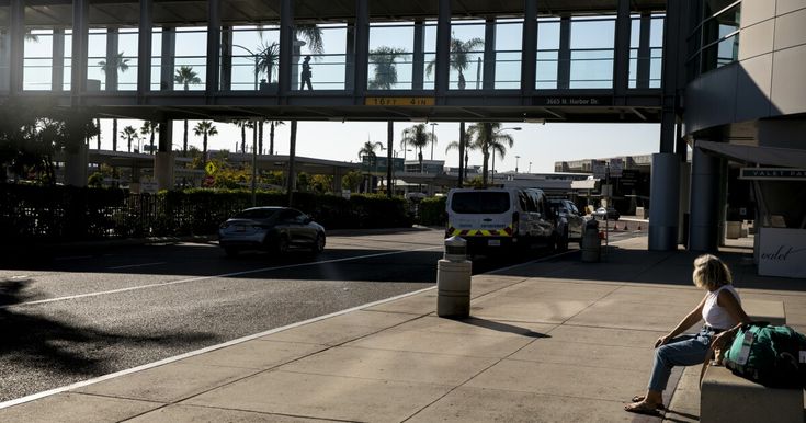 a woman sitting on a bench in front of an overpass with cars passing by