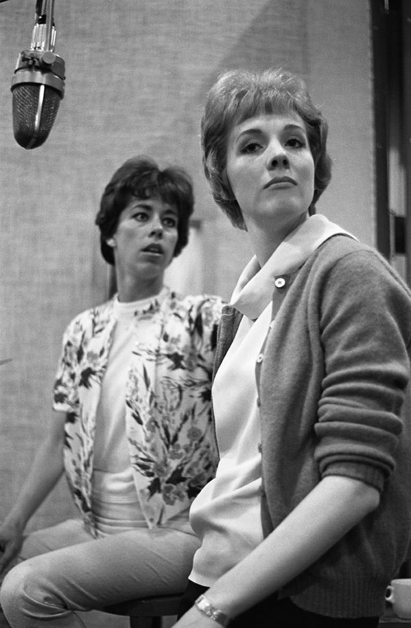 black and white photograph of two women sitting in front of a microphone with one woman standing behind her