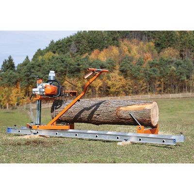 a log being operated by a chainsaw on a field with trees in the background