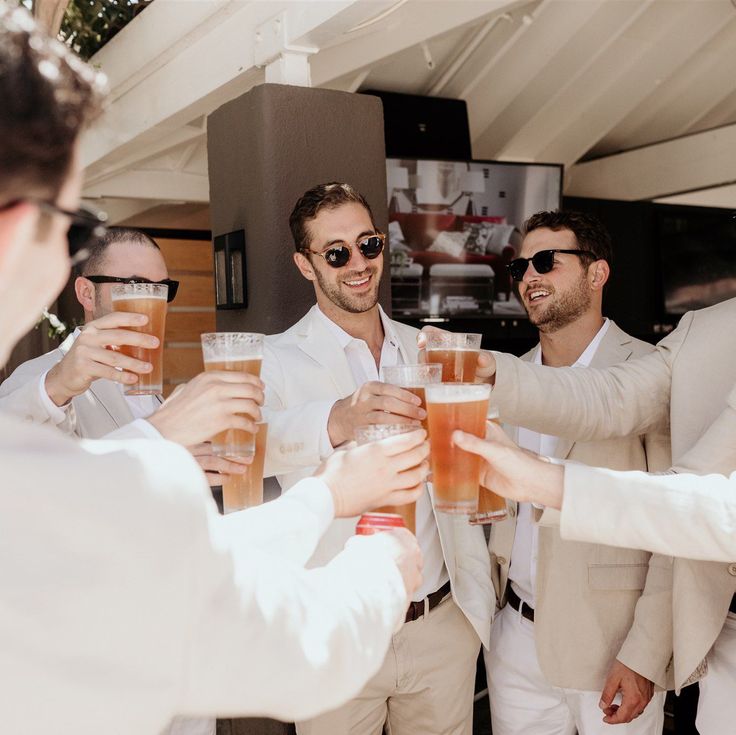 a group of men in white suits toasting with beer glasses on their hands and smiling at the camera