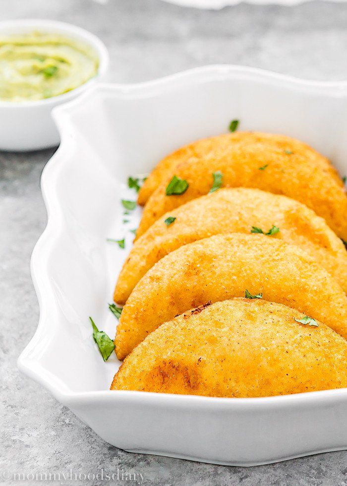 some fried food in a white bowl on a table next to dips and sauce