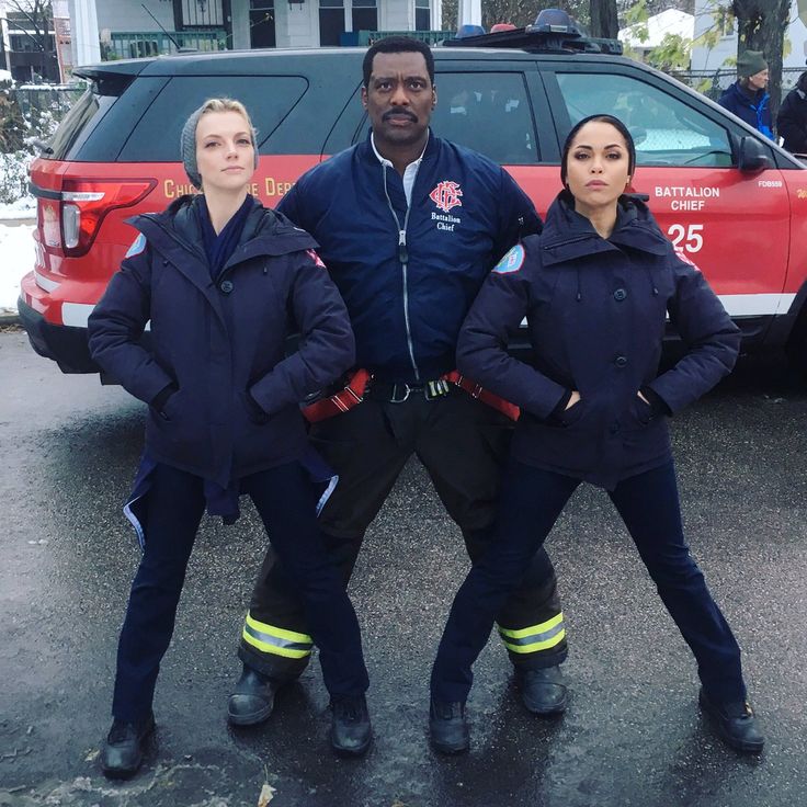 three fire fighters standing in front of a red truck with their arms around each other