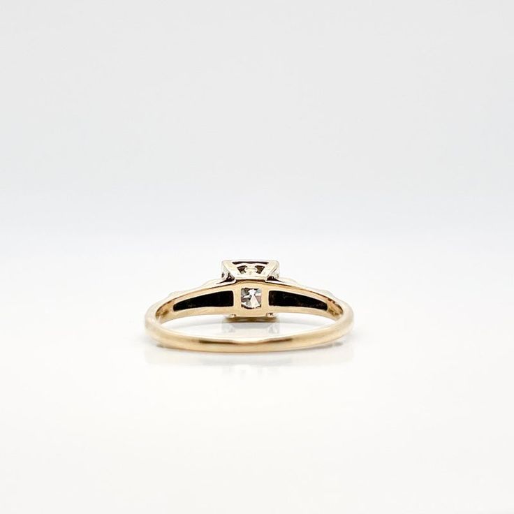 a yellow gold ring with a diamond on the top and side, sitting on a white surface