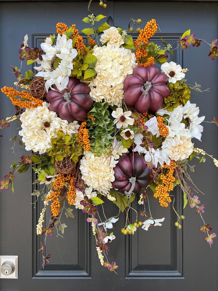 a wreath with pumpkins and flowers hanging on a door