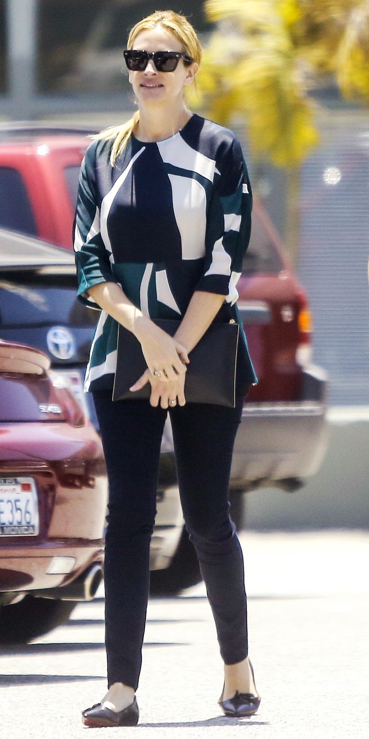 a woman in black and white shirt standing on street next to parked cars with sunglasses on