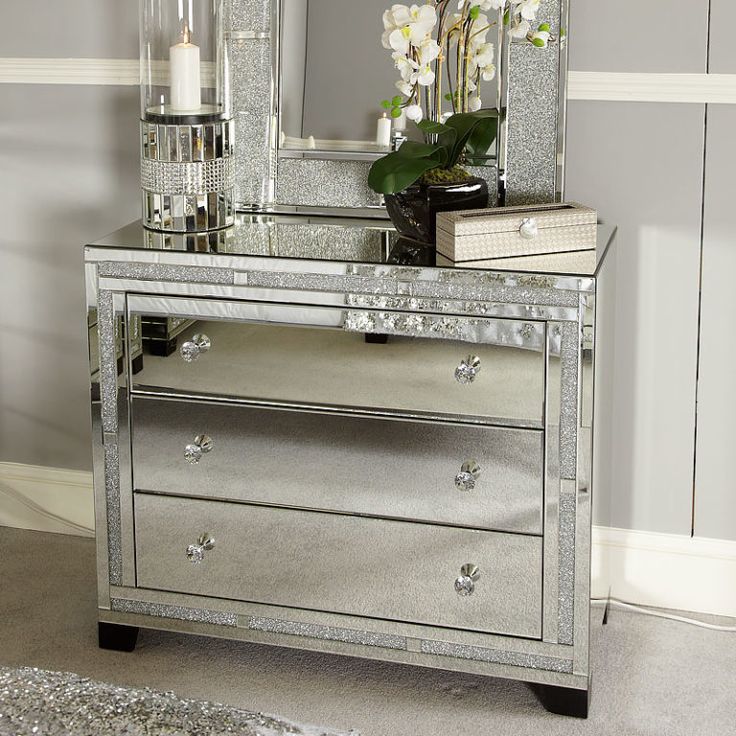 a silver mirrored dresser with flowers and candles on the top, in front of a gray wall