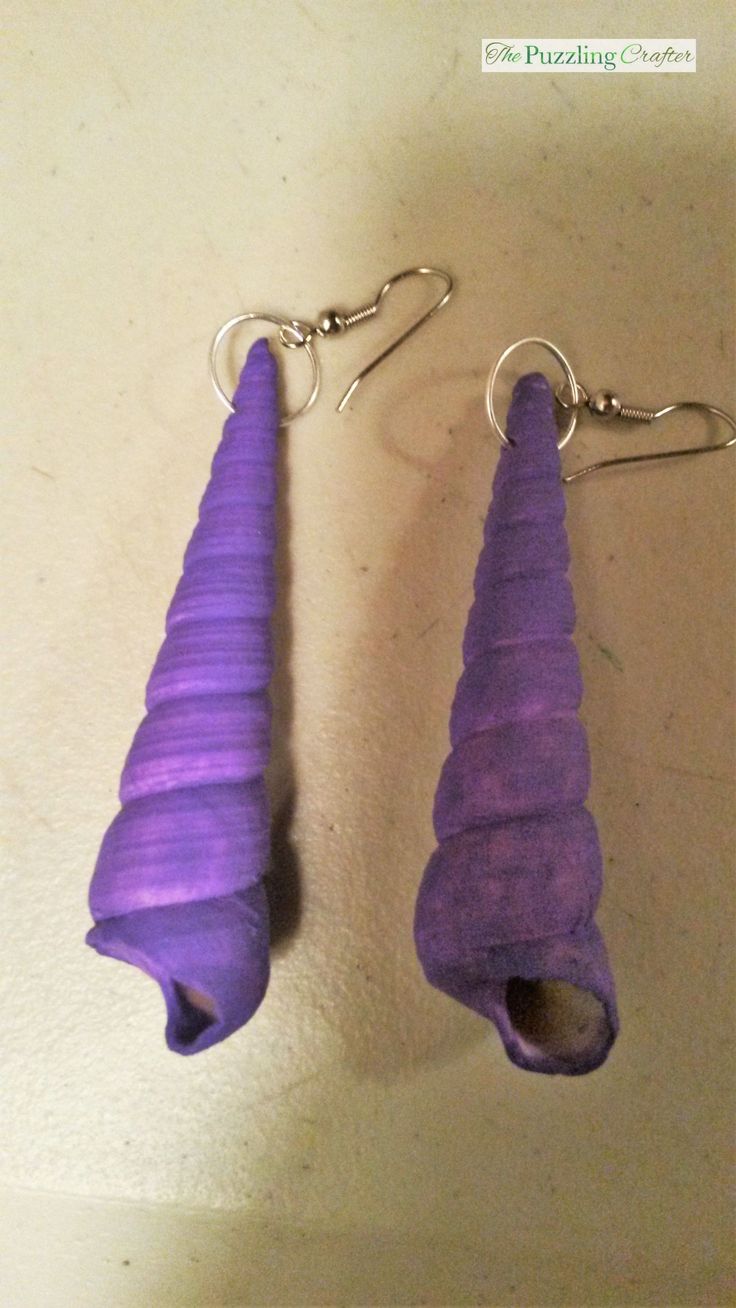 two purple earrings hanging from hooks on a table