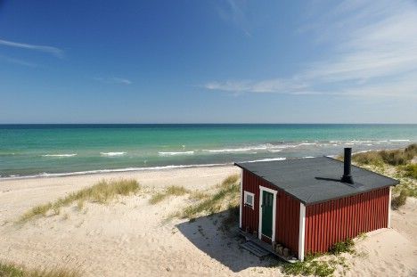 a small red building sitting on top of a sandy beach next to the ocean,