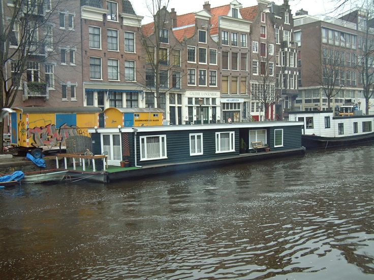 two houseboats are docked on the water in front of some brick buildings and trees