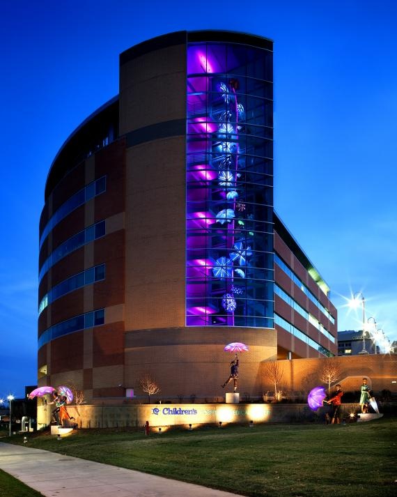 a large building with purple lights on it's side and people walking in the grass