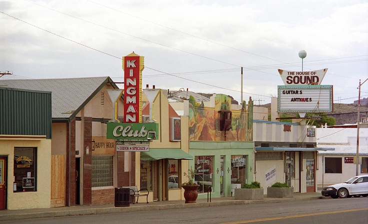 an old town with many stores and cars parked on the side of the road in front of it