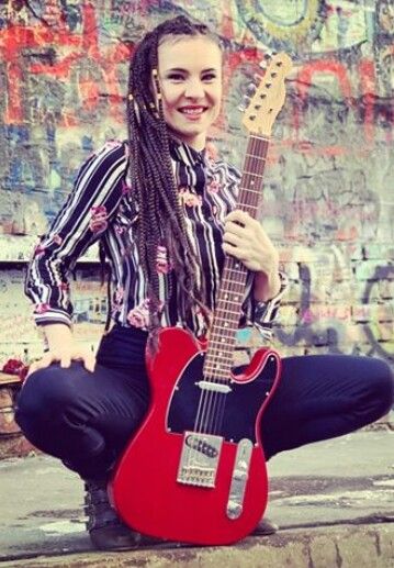 a woman with dreadlocks is holding a red guitar