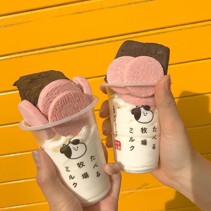 two people holding up ice creams in front of a yellow wall with writing on it