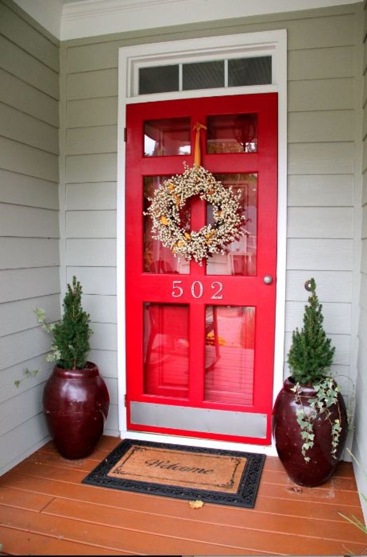 a red front door with a wreath and two planters on the porch next to it