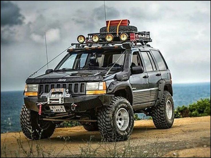 a black four - doored suv parked on top of a dirt road next to the ocean