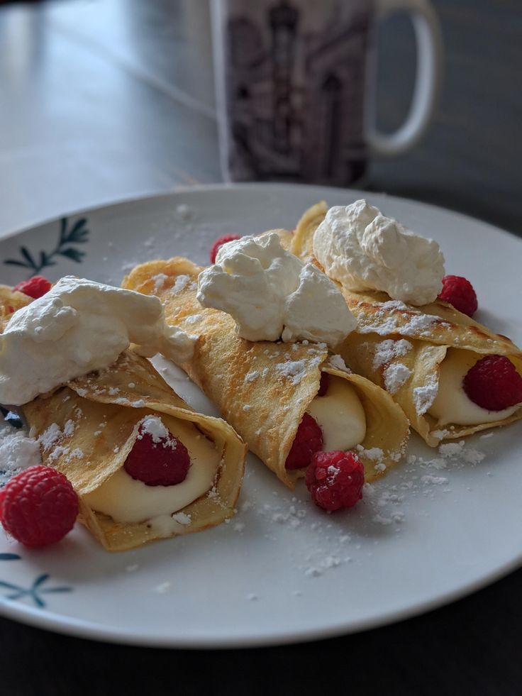 crepes topped with whipped cream and raspberries on a plate next to a cup