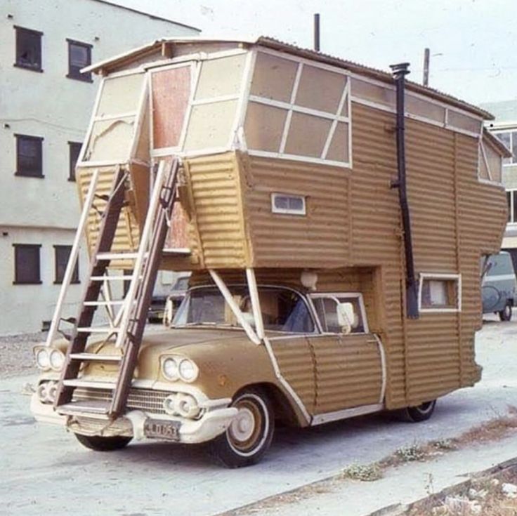 an old car is parked in front of a house with a ladder attached to it