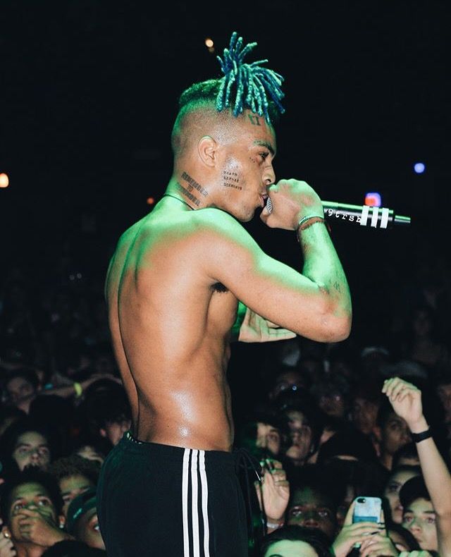 a shirtless man with dreadlocks on his head holding a microphone in front of a crowd