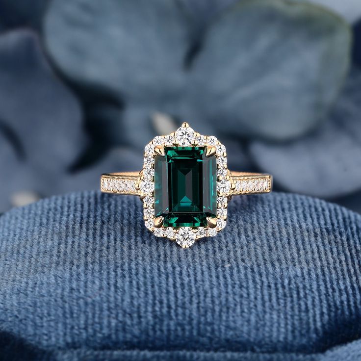 an emerald and diamond ring sitting on top of a blue velvet cushion with flowers in the background