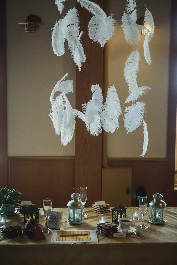 a table topped with lots of white feathers hanging from it's ceiling above glasses