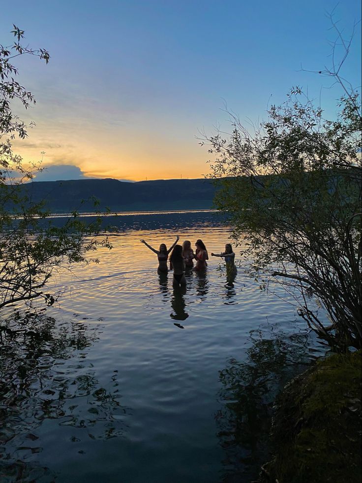 several people are wading in the water at sunset