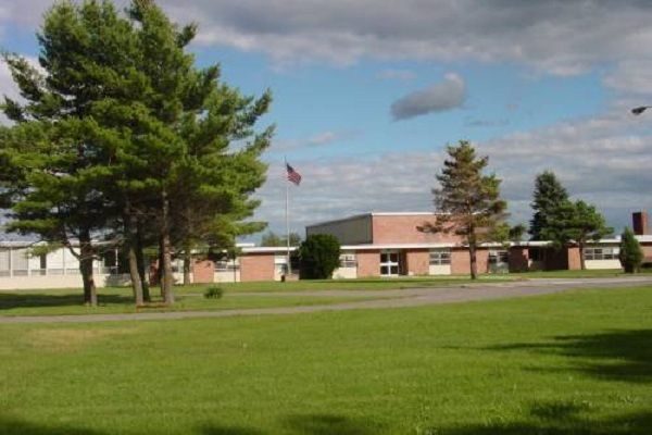 an empty field in front of a building with trees on the side and a flag flying