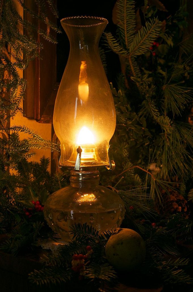 a glass vase with a light in it sitting next to pine cones and evergreens