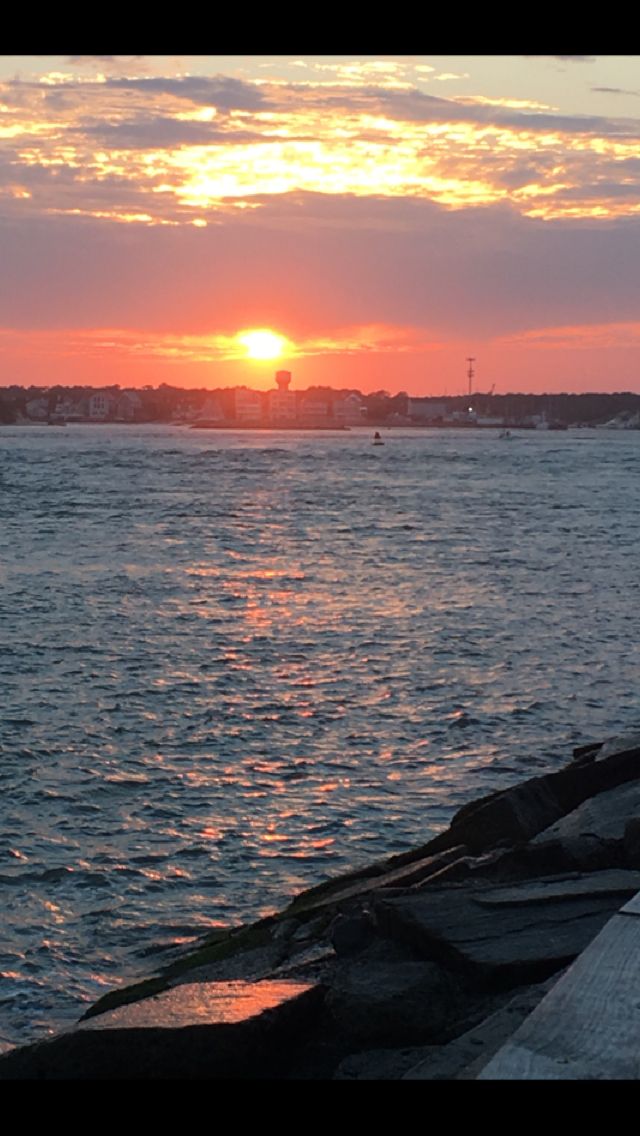 the sun is setting over the water with boats in the distance