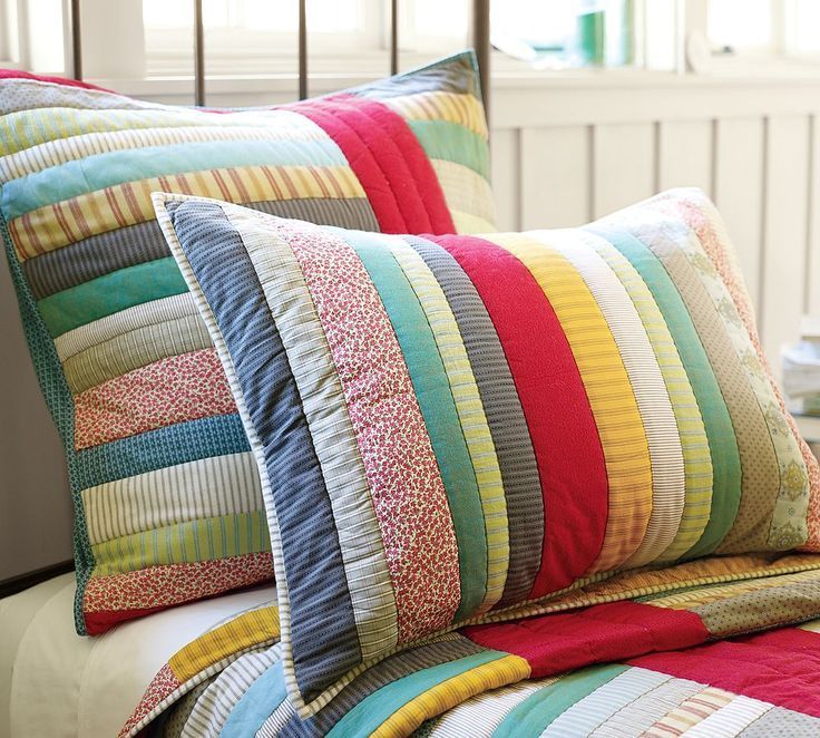 a bed topped with lots of pillows next to a white headboard and window sill