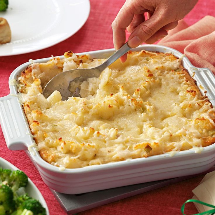 a person cutting into a casserole dish with broccoli in the background