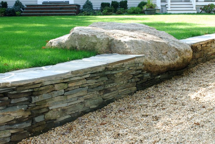 a large rock sitting on top of a grass covered field next to a stone wall