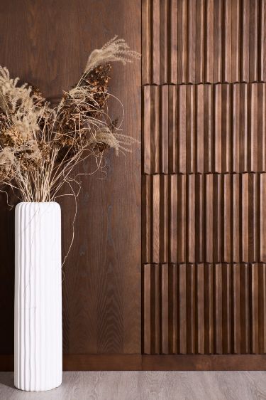 a tall white vase with dried plants in front of a wood paneled wall and floor