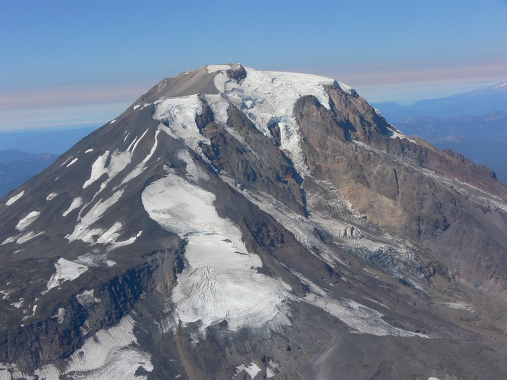 an aerial view of a mountain with snow on it's summit and mountains in the background