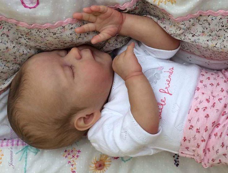 a baby laying on top of a bed next to a white blanket with pink flowers