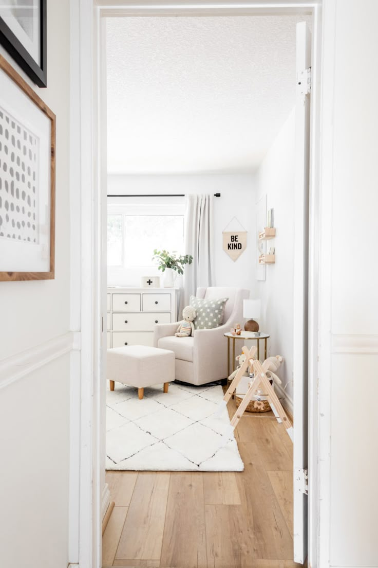 an open door leading to a living room with white furniture and wood floors in it