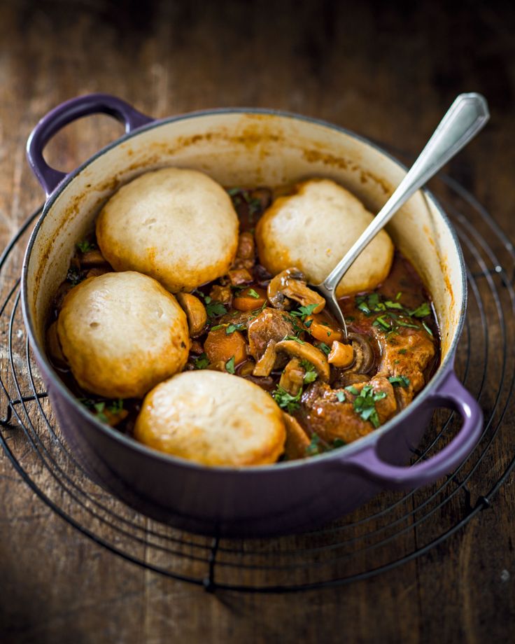 a pot filled with stew and dumplings on top of a wire rack next to a wooden table