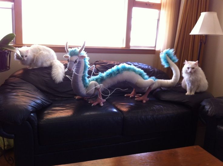 two cats are sitting on the couch and one cat is looking at the dragon statue