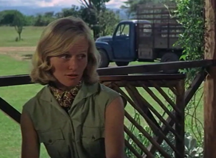 a woman sitting on a porch in front of a blue pick up truck and looking off into the distance