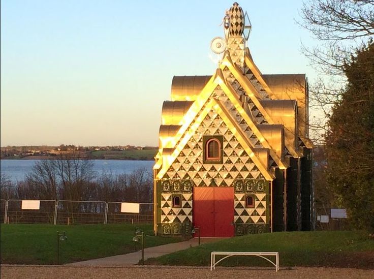 a small church with a red door in the middle of a grassy area next to water