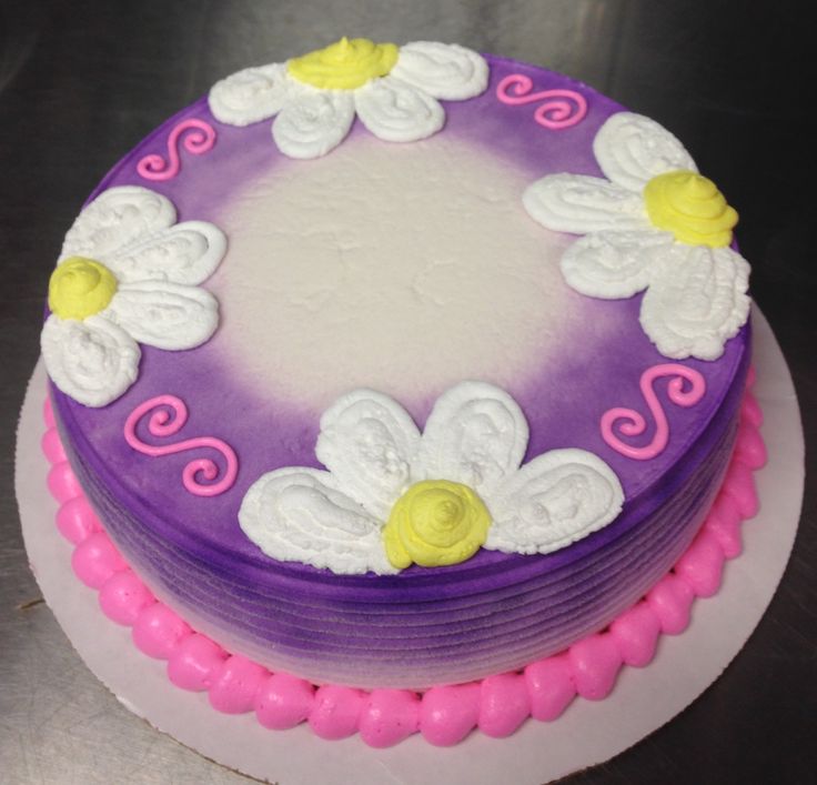 a cake with white and purple frosting on a silver surface, decorated with flowers