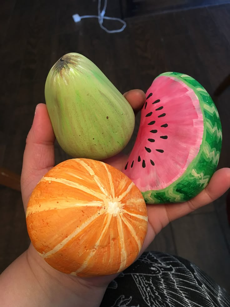 a person holding three pieces of fruit in their hand, including watermelon and an orange