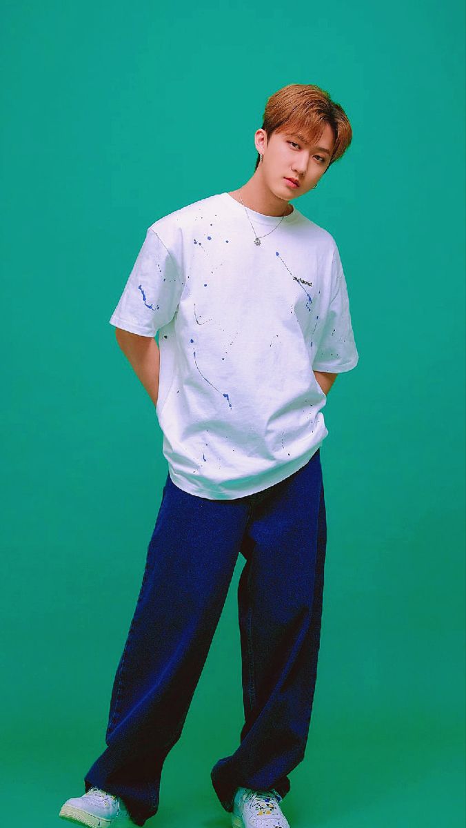 a young man standing in front of a green background wearing blue pants and a white t - shirt